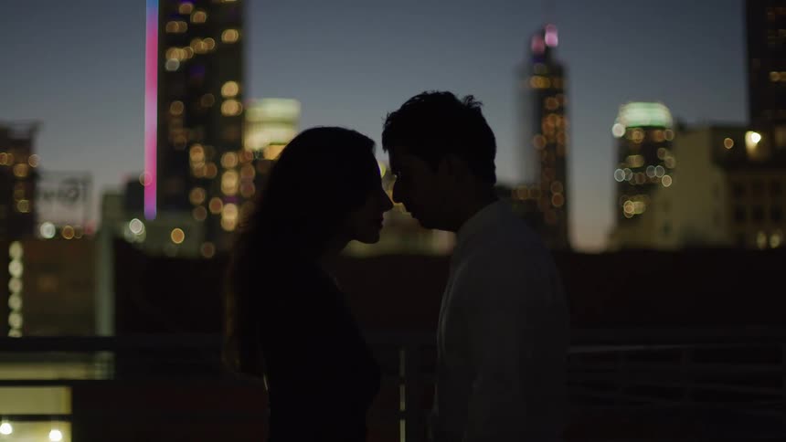 Silhouette of a couple putting their heads together with buildings in the background