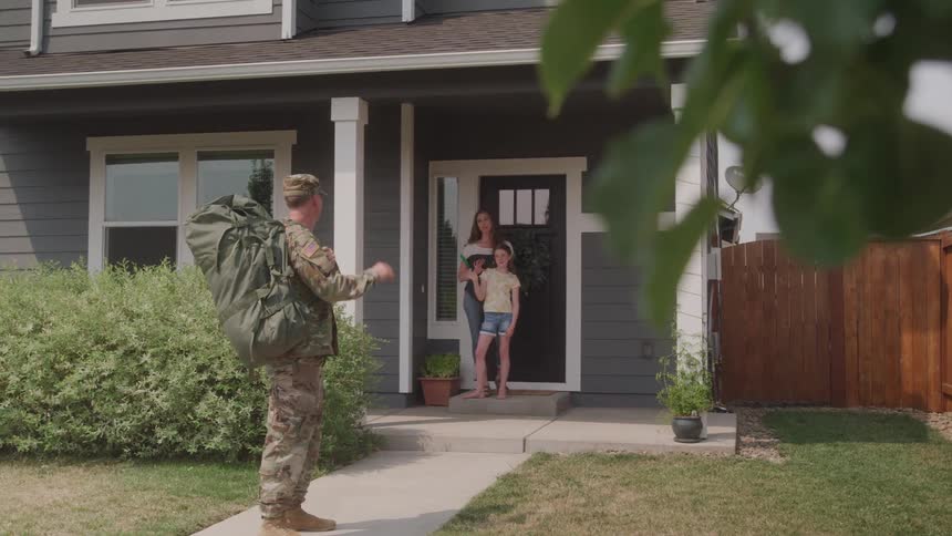 A soldier says goodbye to his family outside their home before deployment