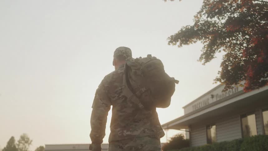 A military man places his bag over his shoulder while walking through a walkway in a city during daytime