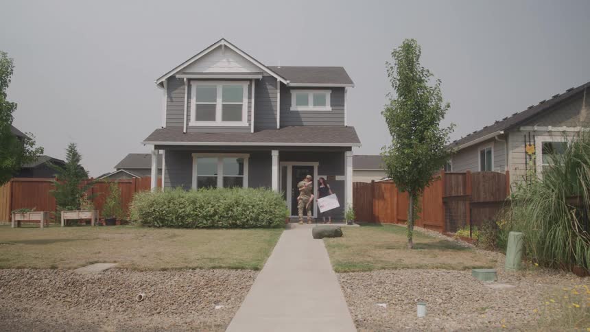 A male soldier runs and embraces his family expecting him in front of their home during daytime