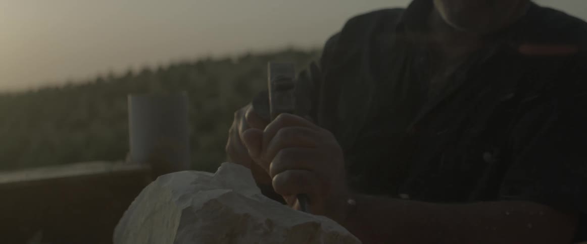 A man chisels a chunk of wood outside
