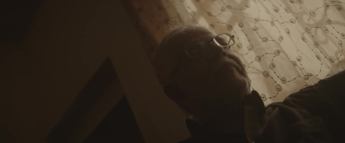 A man wearing glasses sits next to a window