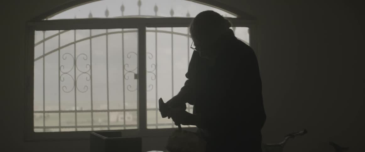 An elderly man works with a hammer and chisel
