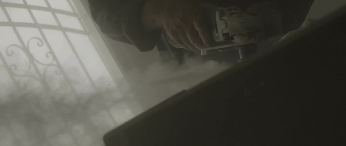 A man uses a tool to grind a rock while dust flies through the air