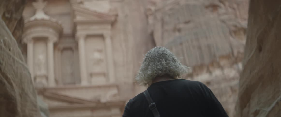 A man approaches a building that is carved into a canyon wall