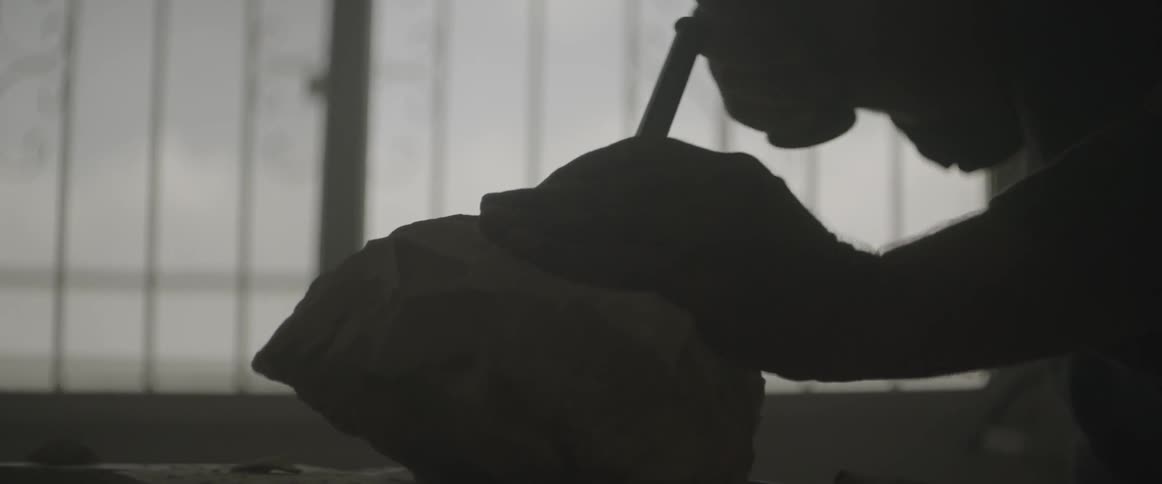 A man uses a chisel and hammer on a rock
