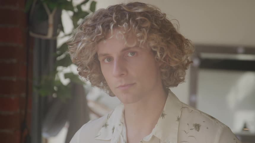 A young man stares into the camera blankly and blinks