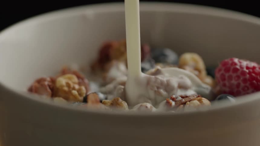 Milk being poured into a bowl with nuts and berries