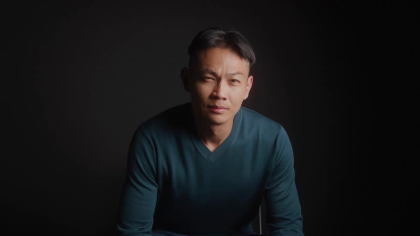 Man sits in dark studio looking into camera