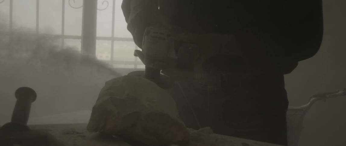 A man works with a grinder on a sculpture