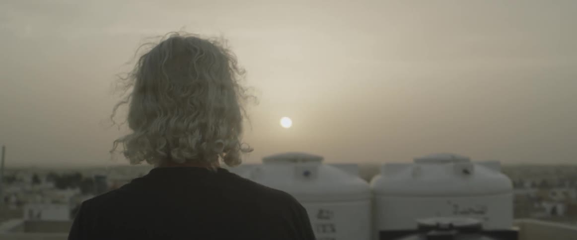 An older man is looking out over a city at dawn or dusk
