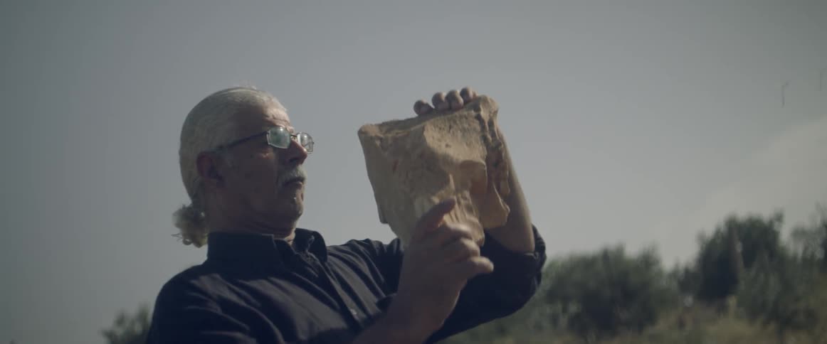 A man holds up a large rock on a clear sunny day