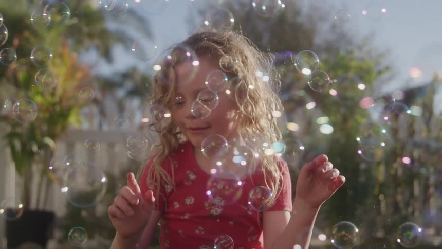A child plays with bubbles on a lawn at midday happy and excited