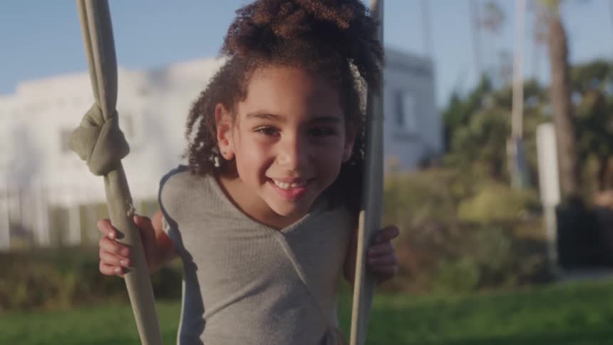A young girl smiles brightly while swinging outside on a sunny day