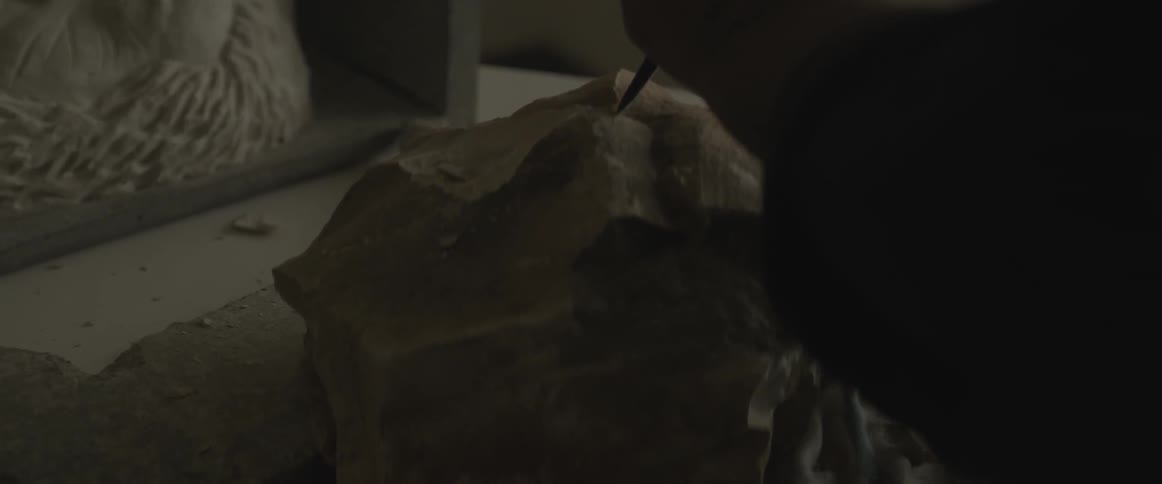 Person chiseling chunk of rock on table indoor