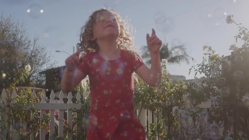 A joyful girl is playing with bubbles outdoors