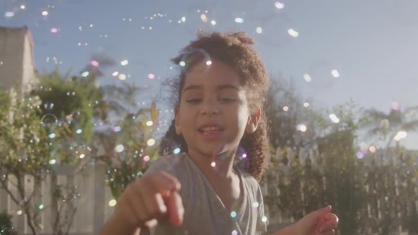 A girl plays with bubbles in a sunlit yard