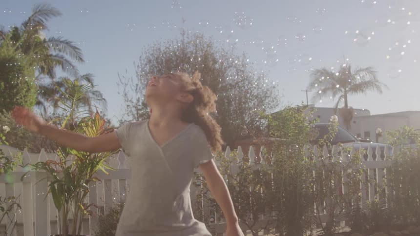 Little girl with curly hair jumping and playing with soap bubbles