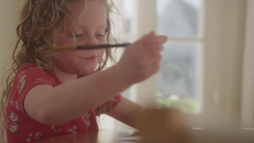 Little girl holding a paintbrush sitting at a table