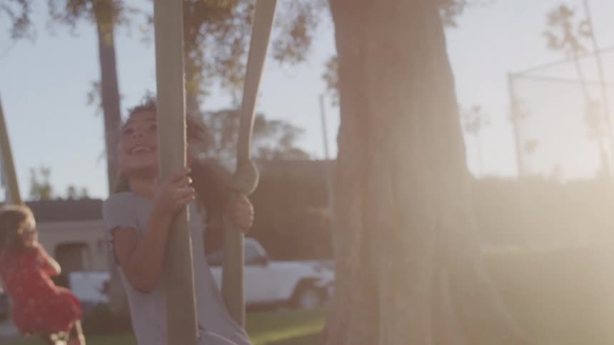 The girls swing from the tree looking up and smiling