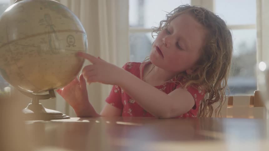 A young girl intently examines a globe pointing to a location with curiosity