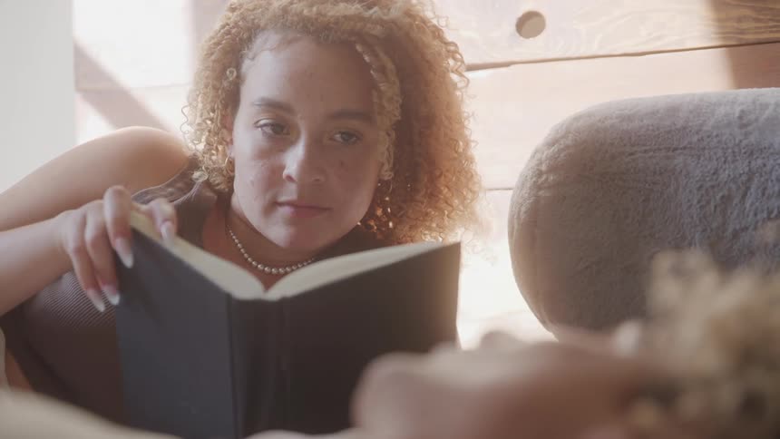Woman reading a book smiles and exchanges glances with the man lying down next to her