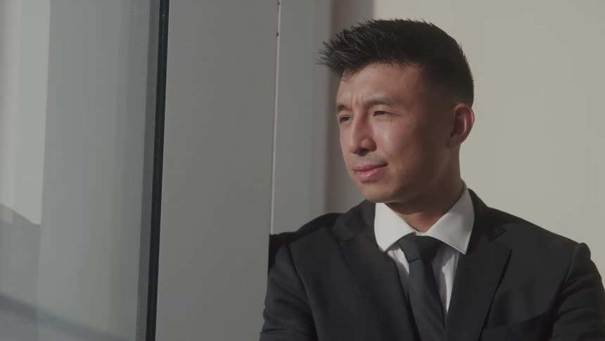 Man in a suit looks thoughtfully out a window in an office setting