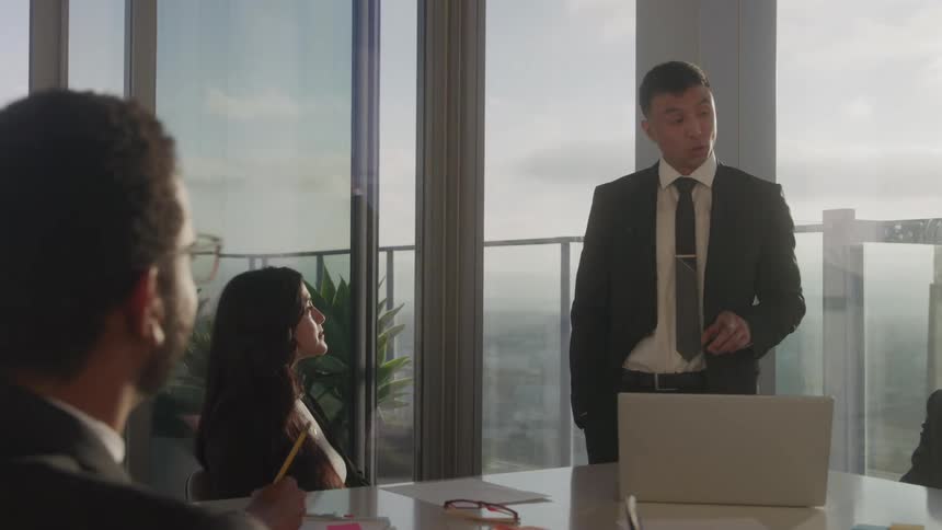 A young businessman stands while speaking to fellow colleagues in a conference room in an office building during daytime