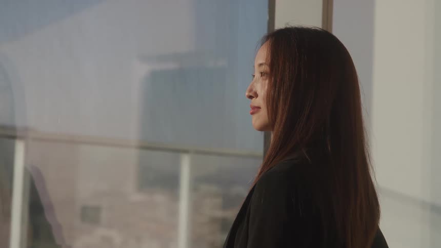 A woman smiles subtly as she looks out a large window of a building