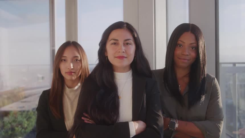 Three women in blazers with their arms crossed in a front room
