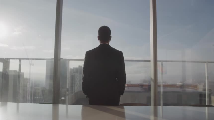 A young businessman looks through a large window while standing in an office building during daytime