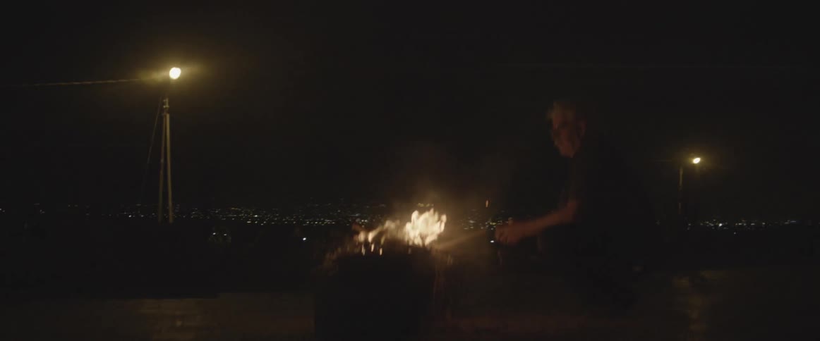 A man sits by an outdoor fire