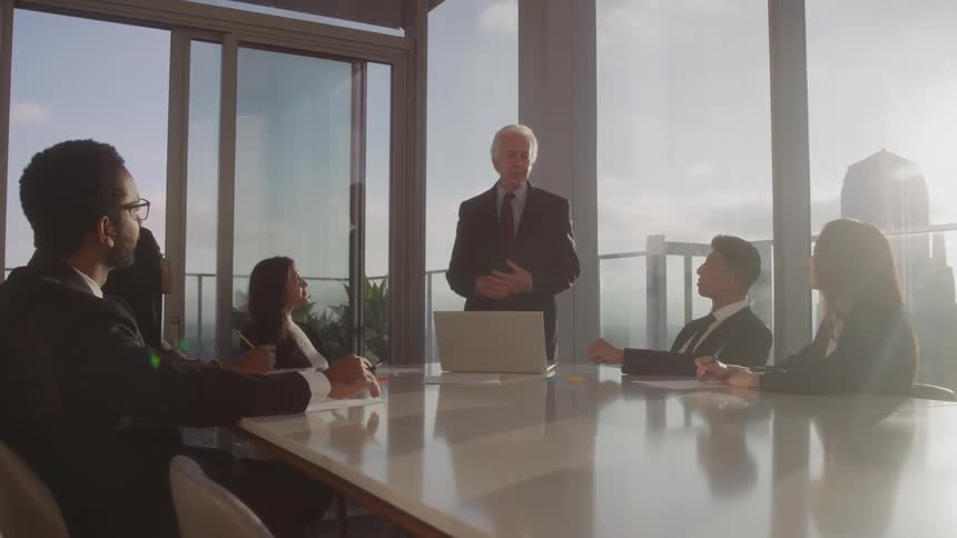 Man standing to lecture to other people sitting at an office desk