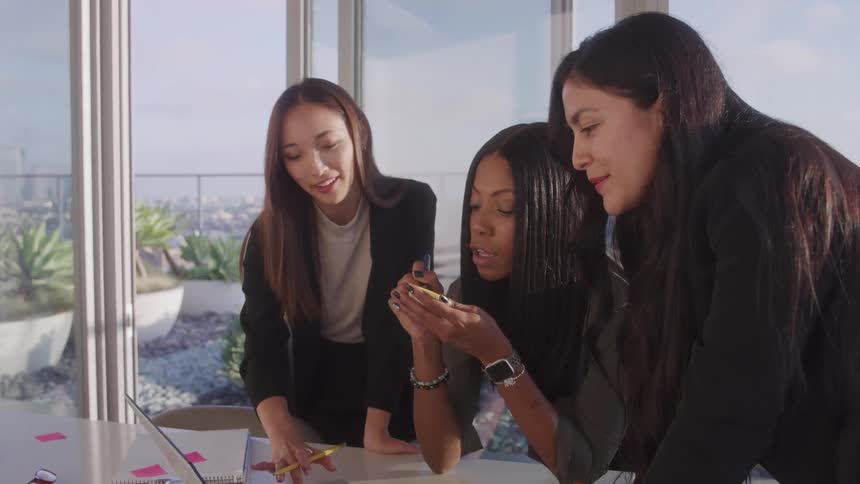 Three businesswomen discuss work while looking at a laptop
