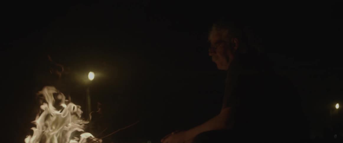 A man is stirring a fire at night
