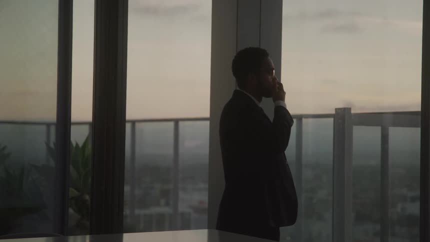 A young black businessman contemplates while walking around indoors in an office at sunset