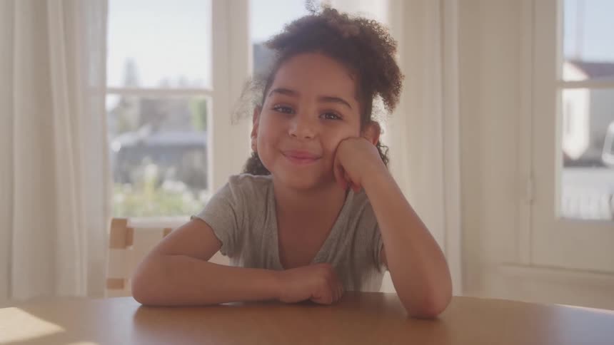 Young girl smiling at the camera while resting her face on her hands