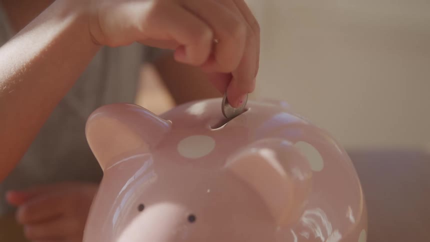 A child hand drops a coin into a piggy bank