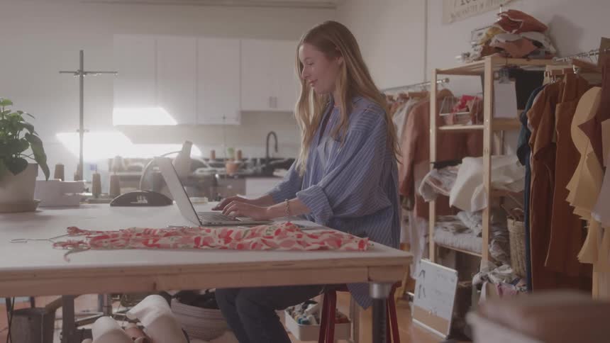 The tailor is using a laptop in her shop