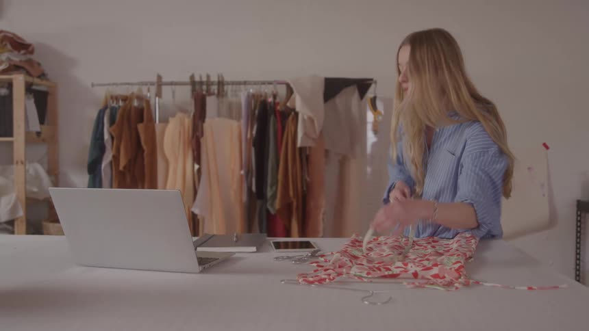 Woman measuring a dress and taking notes on a laptop
