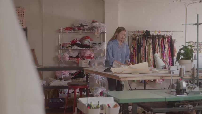 Woman works at cutting table in fabric filled studio