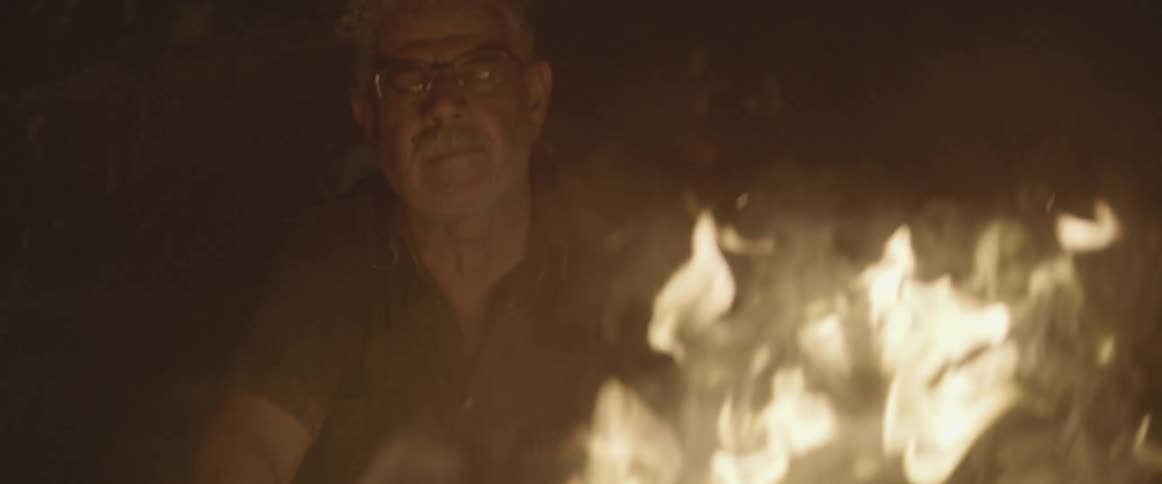 A mustached man looks at a fire