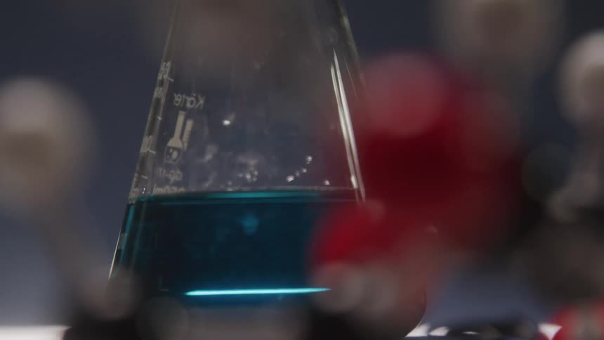 A glass flask is partially filled with a colorful liquid is located in a darkened laboratory