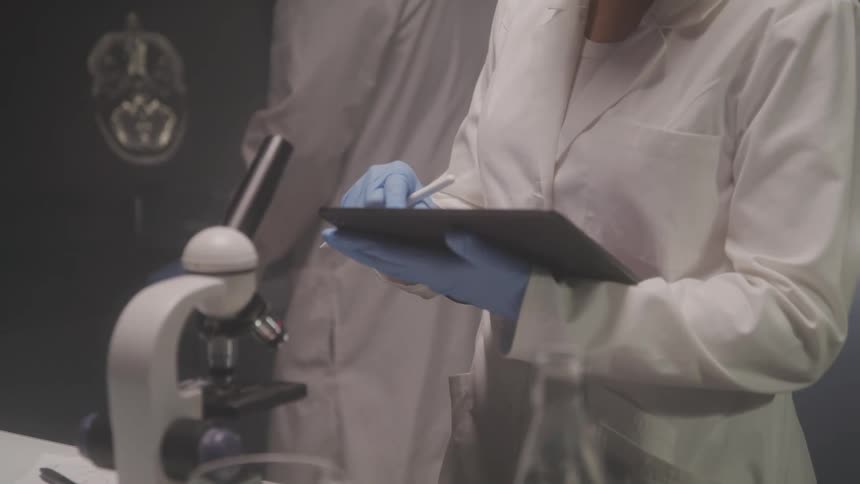 Two people in white coats and gloves interacting with a tablet in a laboratory