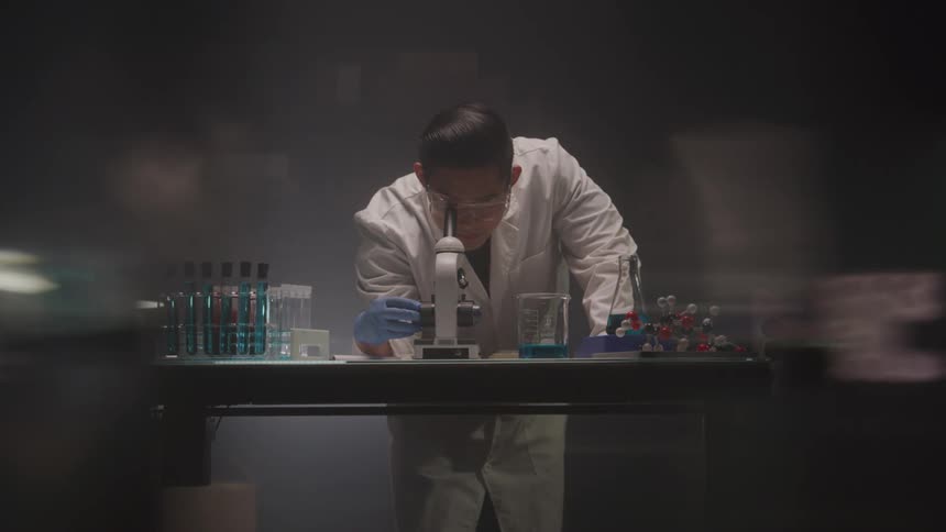 Scientist examines under a microscope in a dimly lit laboratory