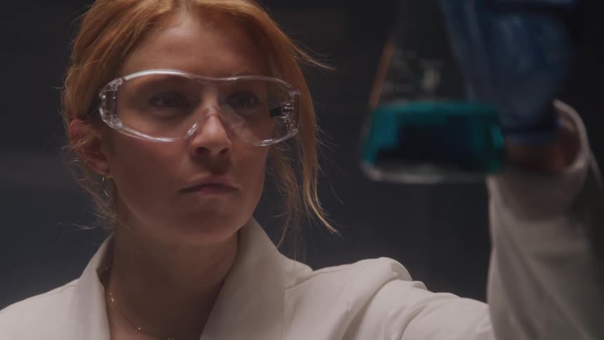 A female scientist inspects a blue liquid in a lab flask in the lab