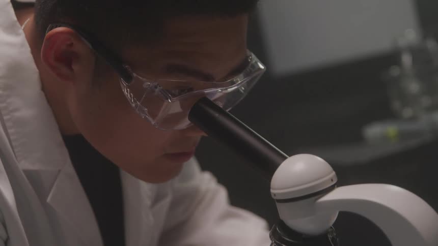 Close up of a male scientist looking through a microscope lens in a lab