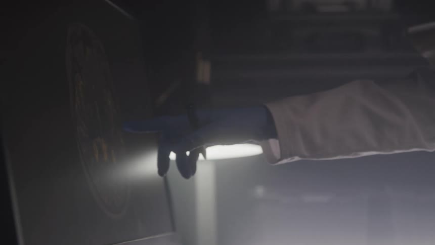 The video shows a person wearing a lab coat and blue gloves holding a tablet and then presenting a circular glowing object with intricate patterns on a dark surface the scene appears to be dimly lit with some illuminated elements