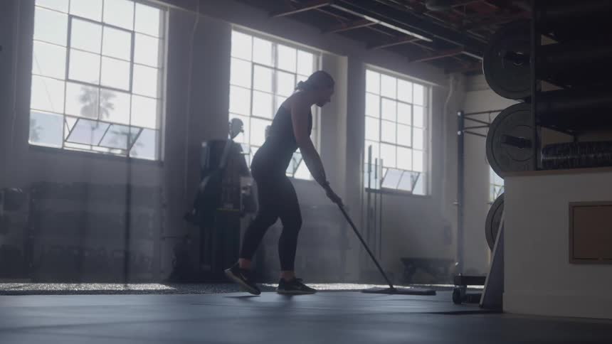 A woman wearing workout clothing is sweeping the floor to a gym