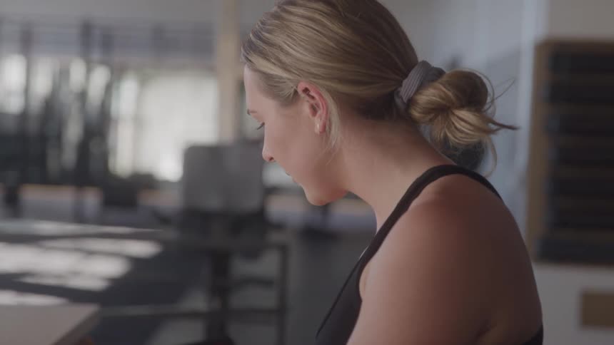 A side profile shot shows a woman with blonde hair tied in a bun wearing a black top she appears to be focused downwards possibly looking at something in front of her with a blurred background suggesting an indoor setting